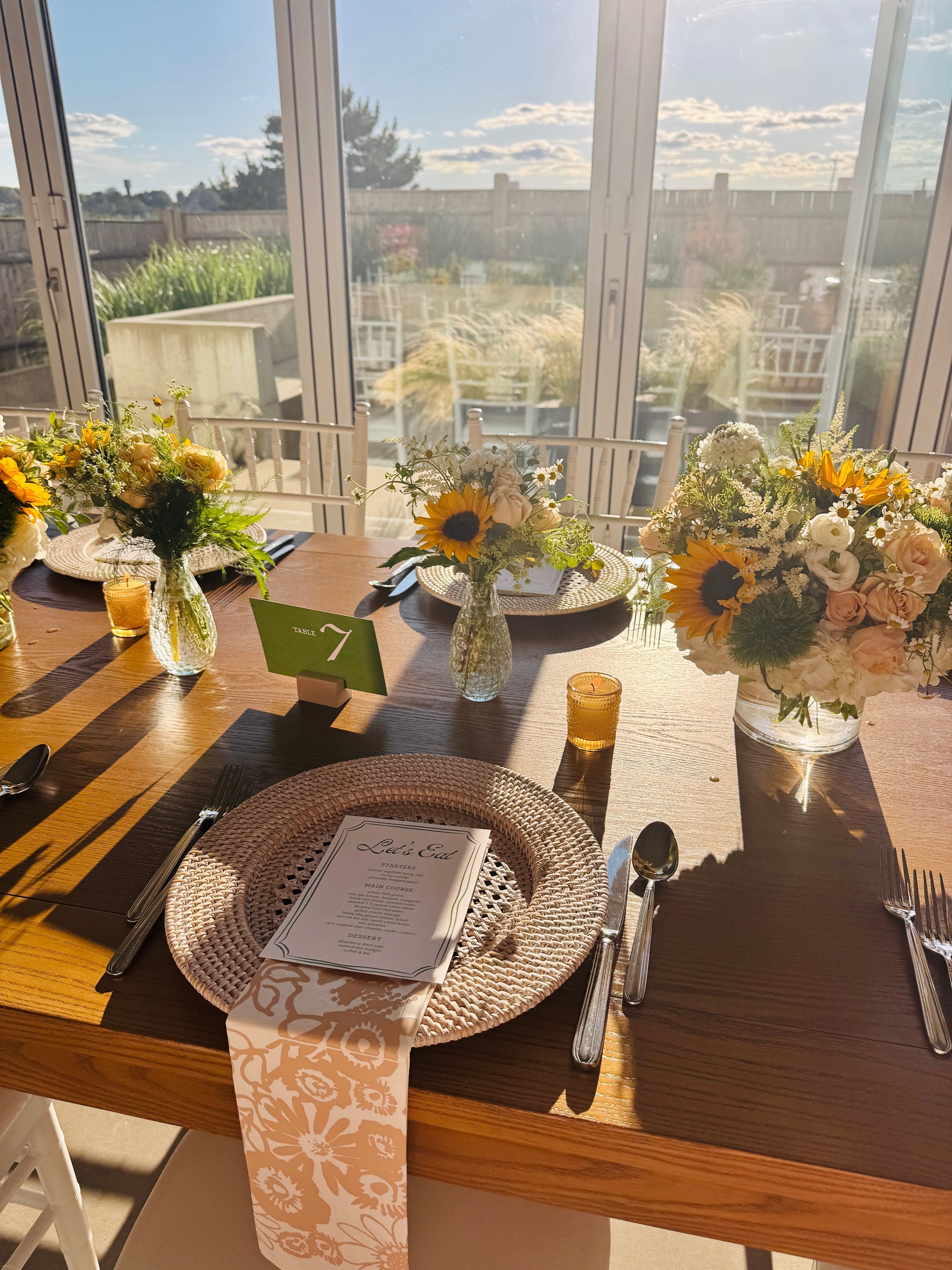 Elegant table setting with sunflowers and floral arrangements by a large window featuring custom napkins by Erin Flett.