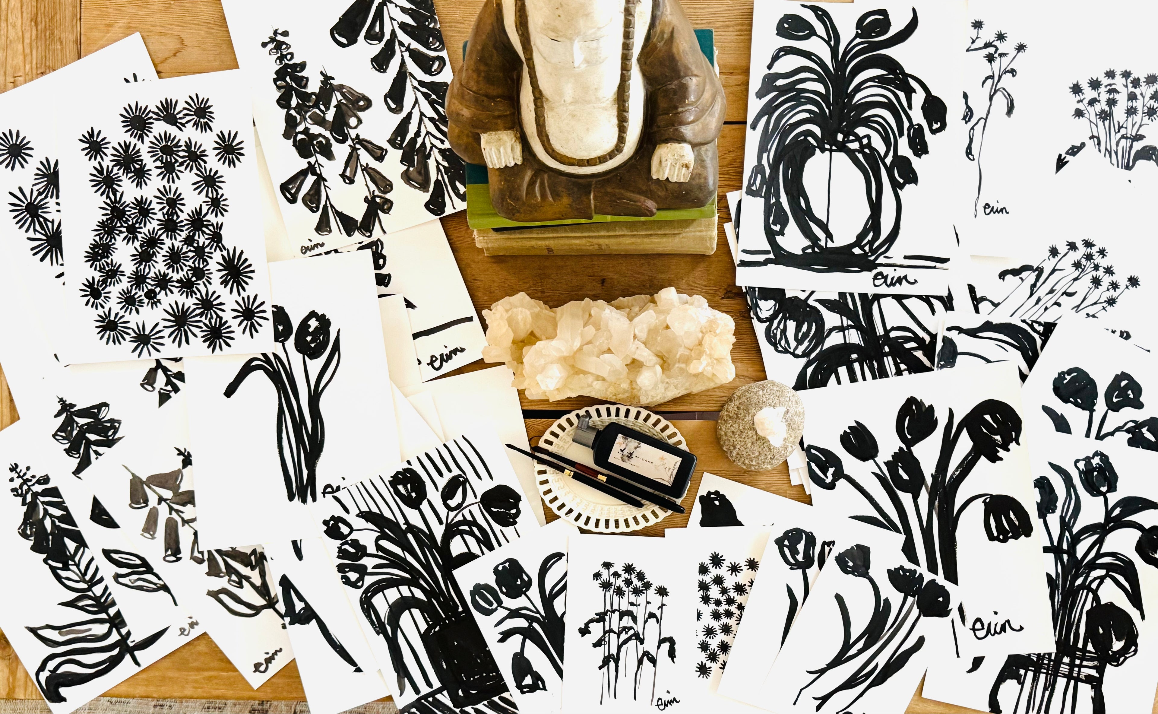 Collage of black and white botanical Erin Flett illustrations on a wooden surface with decorative items.