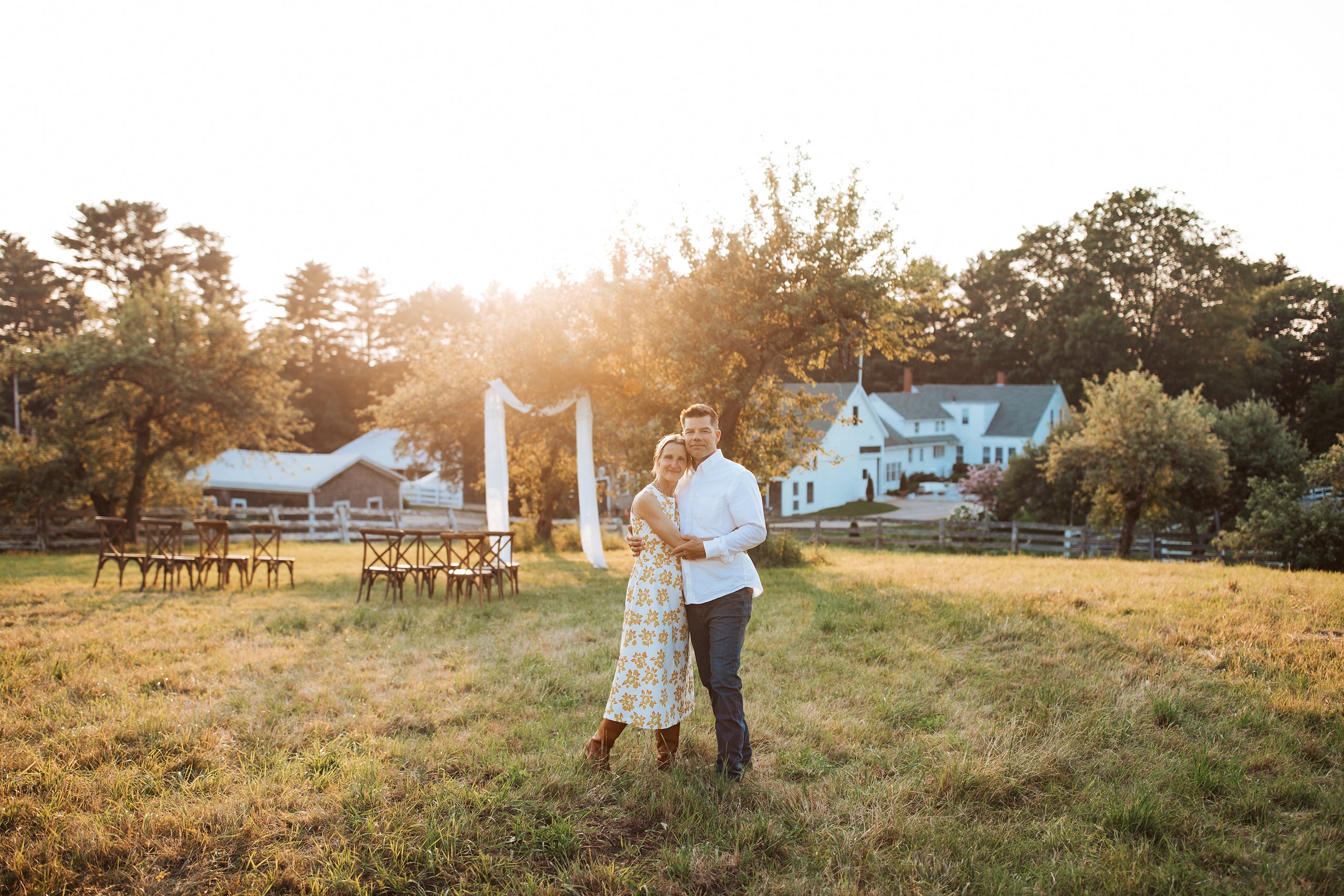 Erin and Maslen Flett standing in a field with a sunset and farm buildings in the background