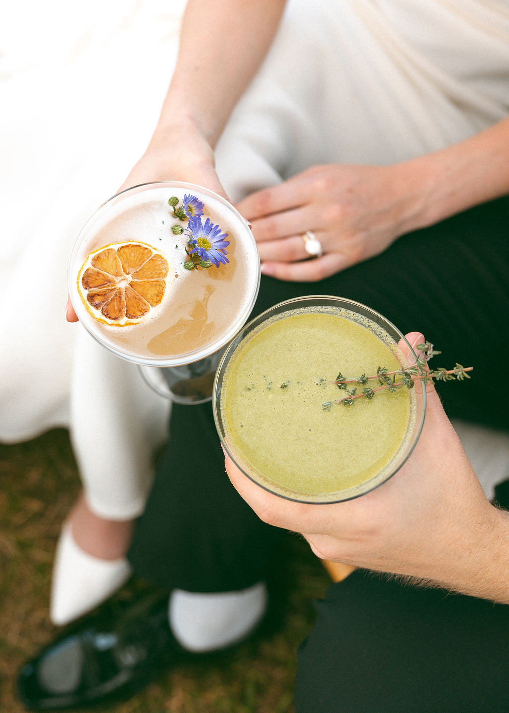 Two people holding drinks with garnishes, one in a white outfit and the other in a black outfit.
